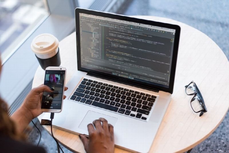 Person testing a mobile app on a phone next to a laptop showing code