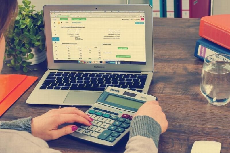 Hands using a calculator next to a laptop showing a spreadsheet