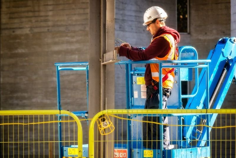 Electrician in a hard hat working from a lift on a building wall