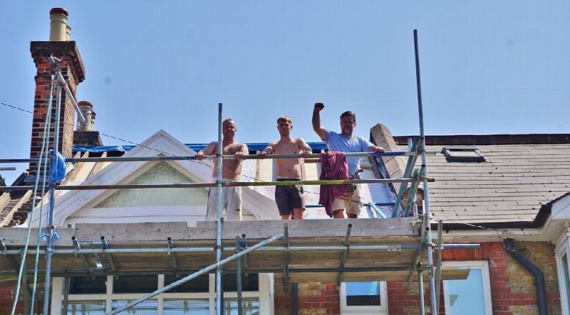 Roofers working on scaffolding along a house roofline