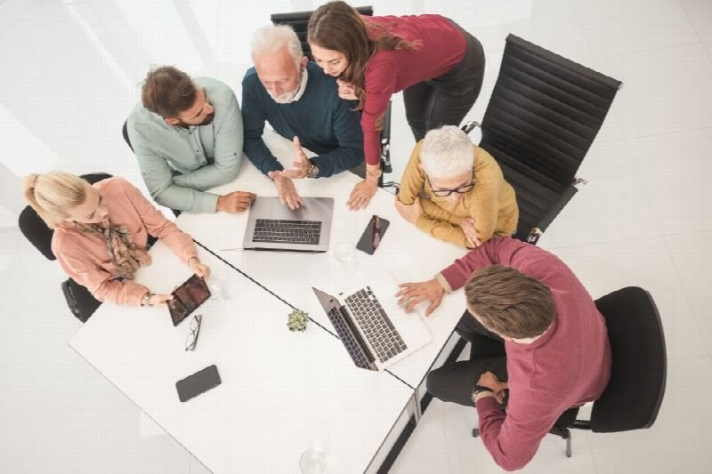 Overhead view of a team meeting around a white conference table with laptops