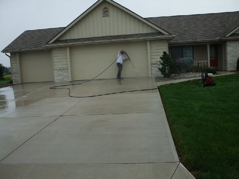 Worker pressure washing a driveway in front of a house