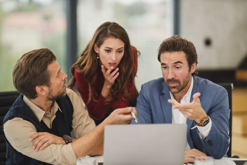 Three colleagues discussing work around a laptop in a bright office